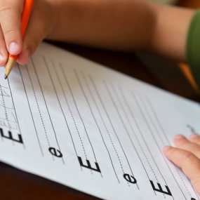 child's hand learning to write in a handwriting book for kids showing the letter E