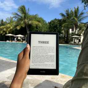 a hand holds up an amazon kindle with a pool in the background