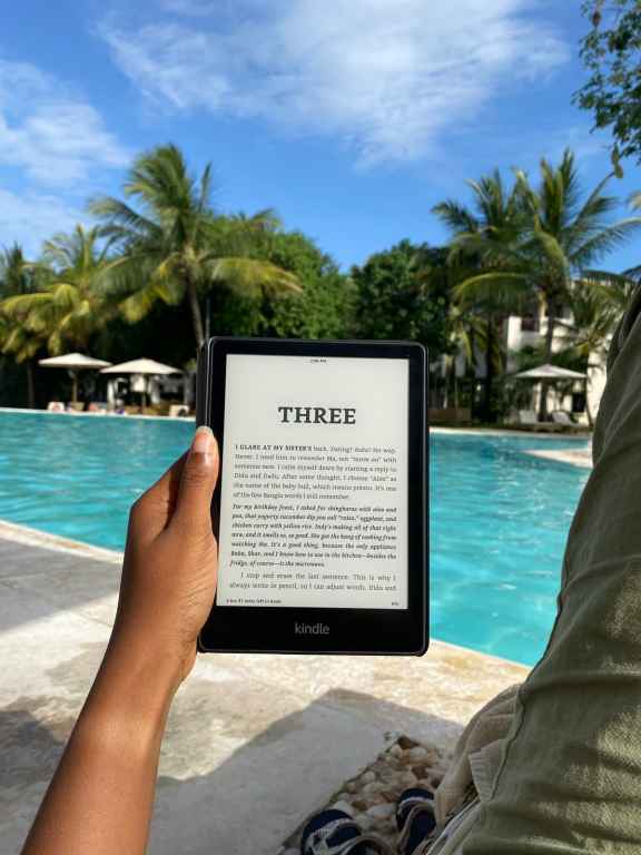 a hand holds up an amazon kindle with a pool in the background