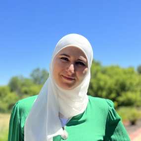 shifa safadi, a woman in white hijab stands outside with blue sky in the background