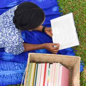 afoma lays on grass with an open book and a basket of books nearby