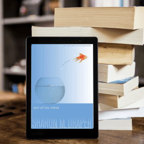 a tablet showing the cover of out of my mind rests on a stack of books