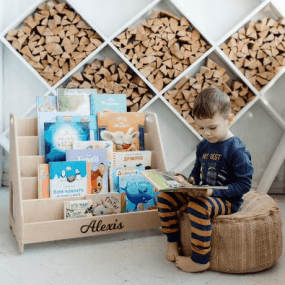 little boy reading next to a wooden bookshelf for kids
